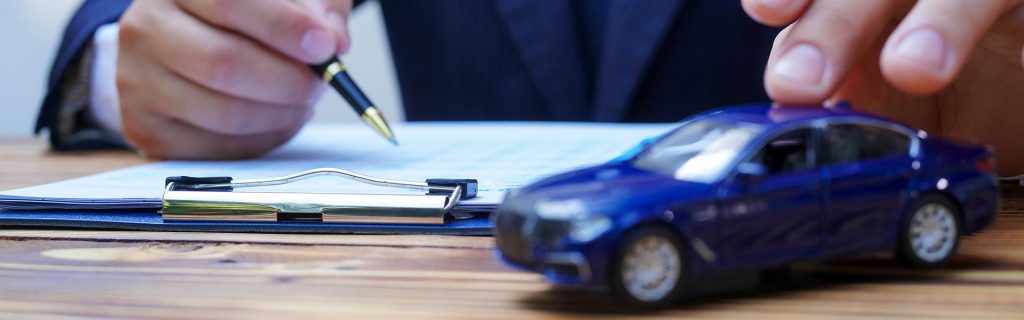 A person in a suit signing a document next to a blue toy car.